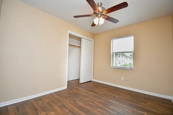 an empty room with wooden floor fan and windows