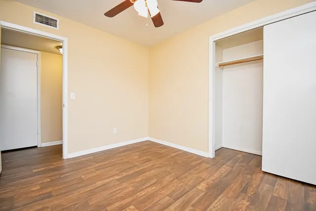 an empty room with wooden floor closet and windows