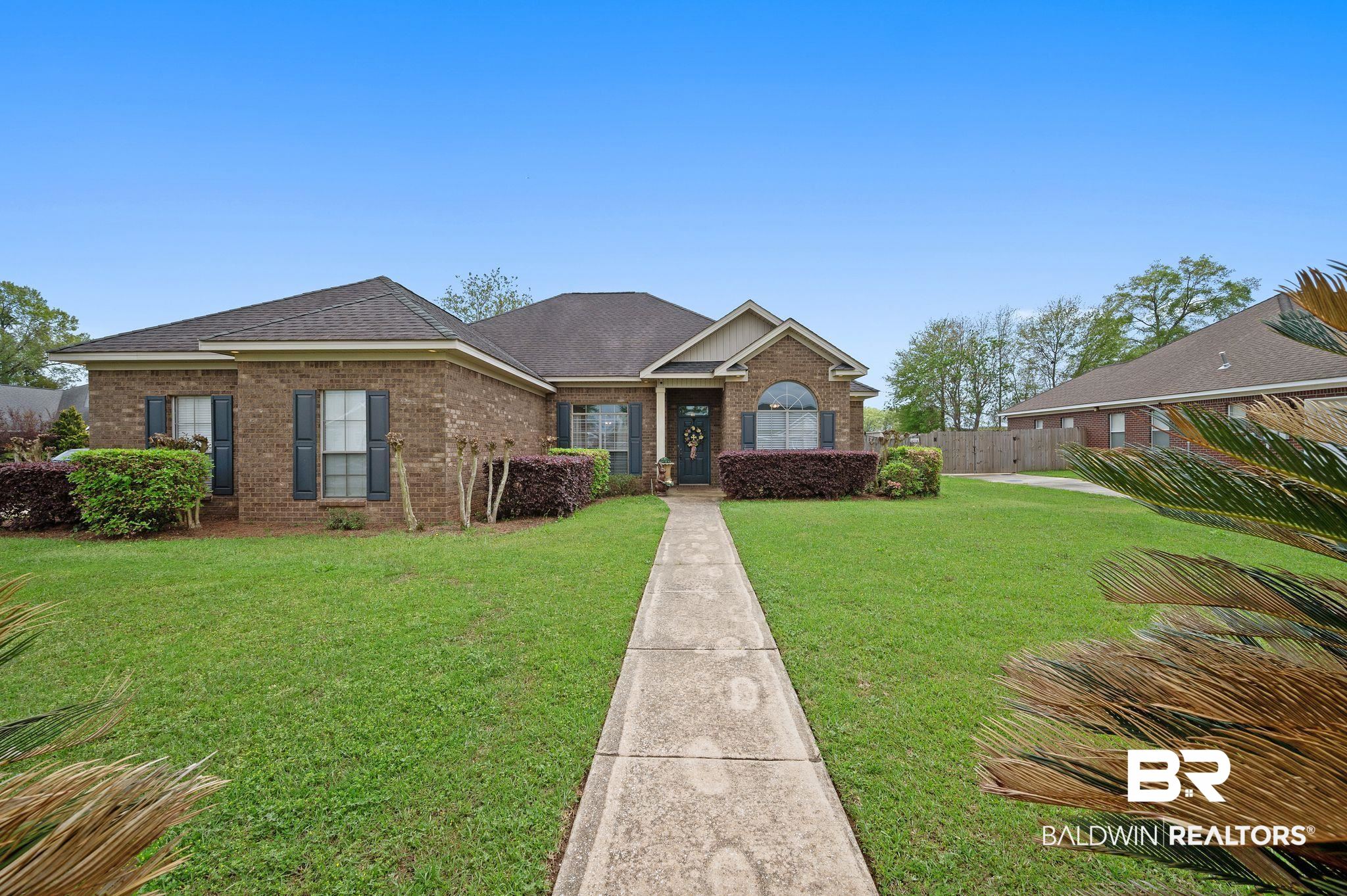 View of front facade featuring a front yard, fence, brick siding, and roof with shingles