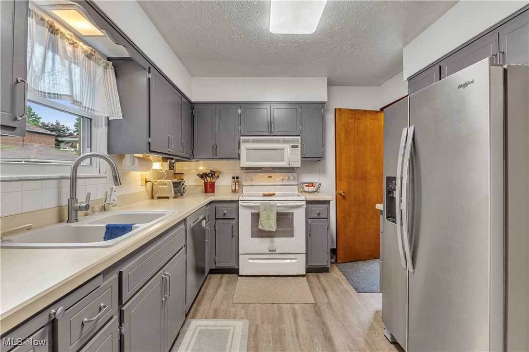 4090 Ridgeview Road Cleveland, OH 44144 - Photo 9 of 40 Kitchen featuring appliances with stainless steel finishes, gray cabinetry, light wood-style flooring, a textured ceiling, and backsplash