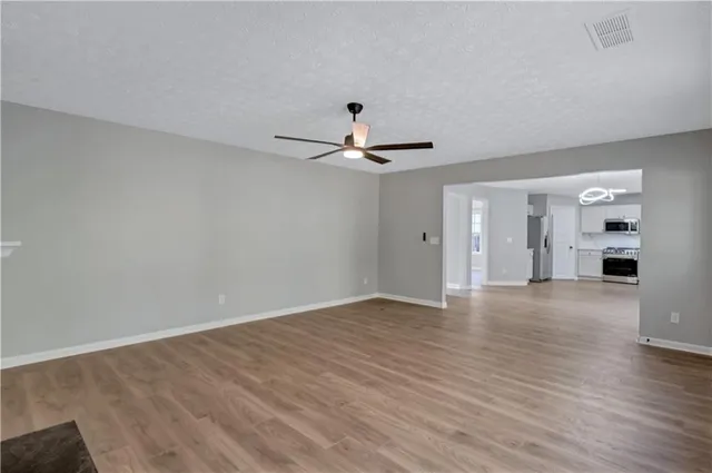 a view of an empty room with wooden floor and a ceiling fan
