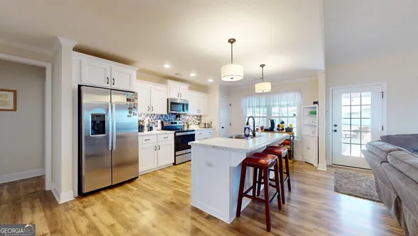 a kitchen with stainless steel appliances kitchen island granite countertop a refrigerator a stove a sink a dining table and chairs with wooden floor