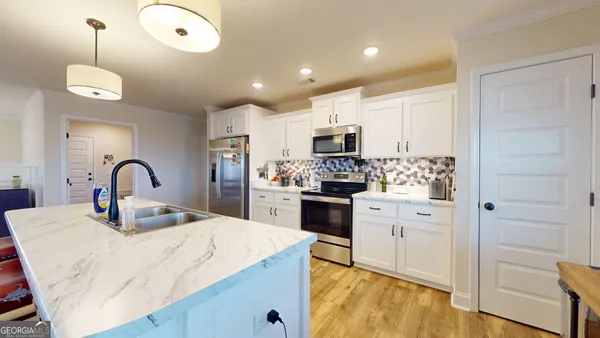 a kitchen with kitchen island granite countertop a stove a sink a refrigerator and white cabinets with wooden floor