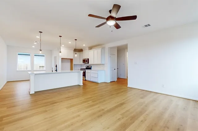 a view of an empty room with kitchen appliances and a ceiling fan