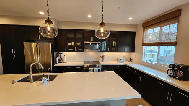 a kitchen with stainless steel appliances a sink a stove a refrigerator a kitchen island with a dining table and chairs