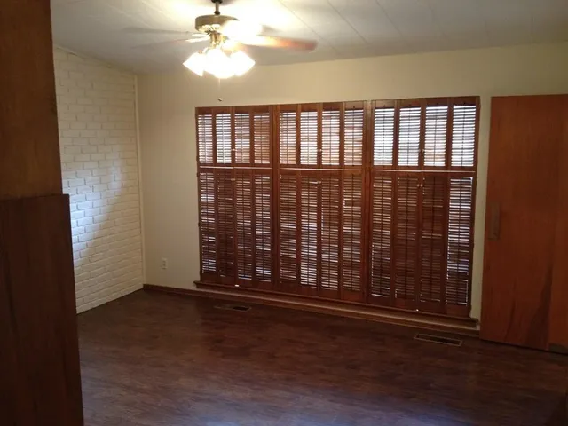 an empty room with wooden floor fan and windows