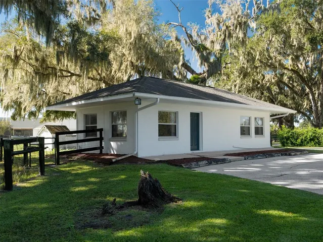 a view of a white house next to a yard with chairs and a tree
