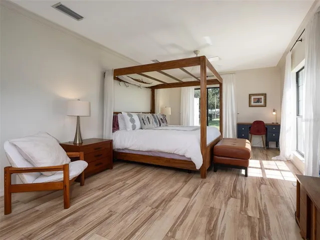 a bedroom with a bed a chair and a potted plant with wooden floor