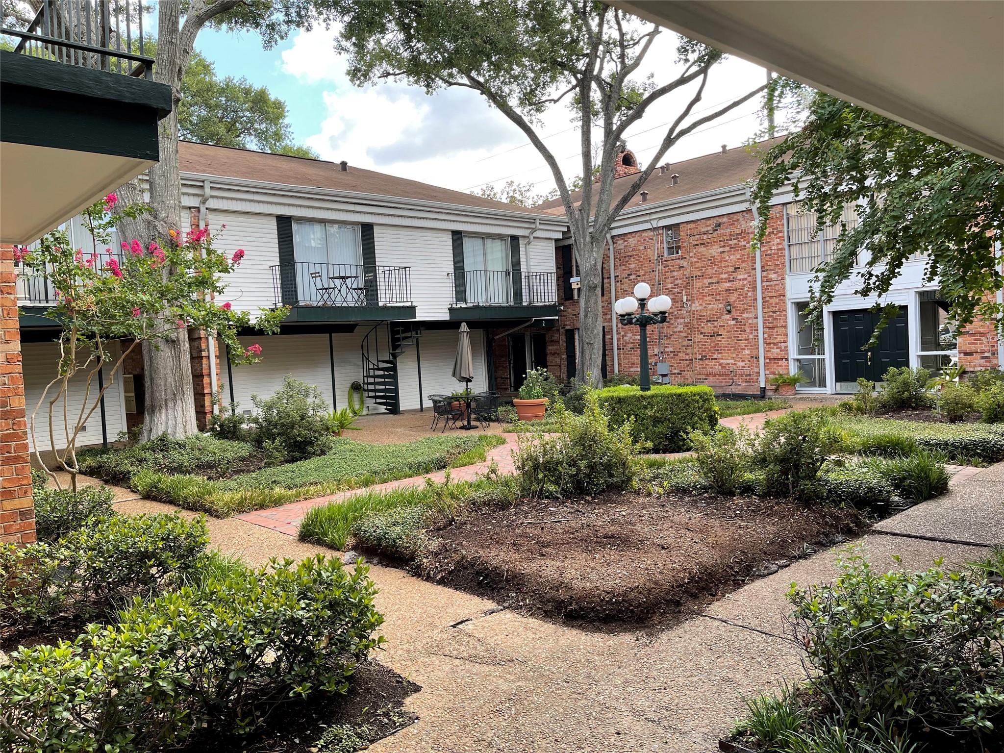3400 Timmons Lane, Unit 13 Houston, TX 77027 - Photo 2 of 17 a view of a white house with a small yard plants and a large tree