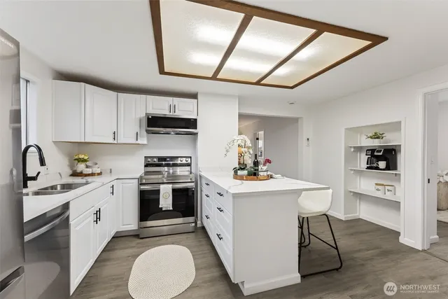 a kitchen with stainless steel appliances granite countertop a stove a sink dishwasher and white cabinets with wooden floor