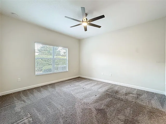 an empty room with ceiling fan and windows