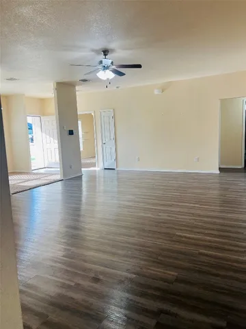 a view of an empty room with wooden floor and a ceiling fan