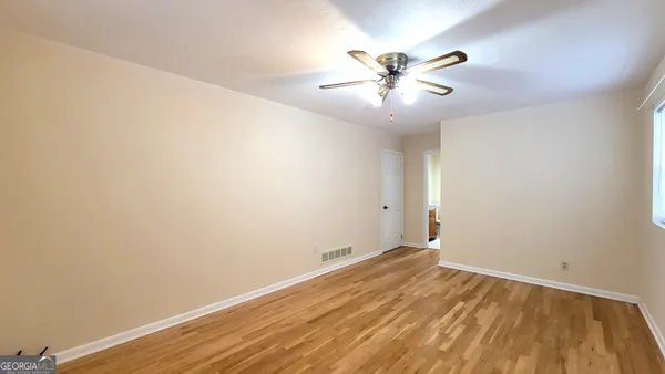 a view of an empty room with wooden floor and a ceiling fan