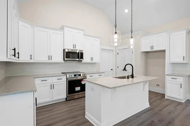 a kitchen with stainless steel appliances granite countertop a sink stove a refrigerator and white cabinets with wooden floor