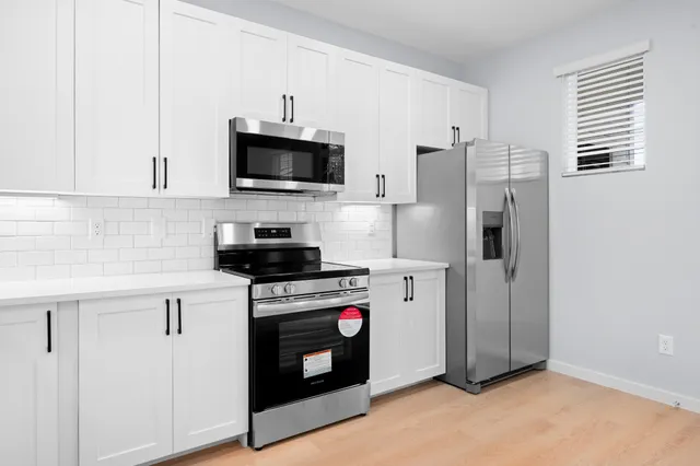a kitchen with stainless steel appliances a stove a refrigerator a sink and white cabinets