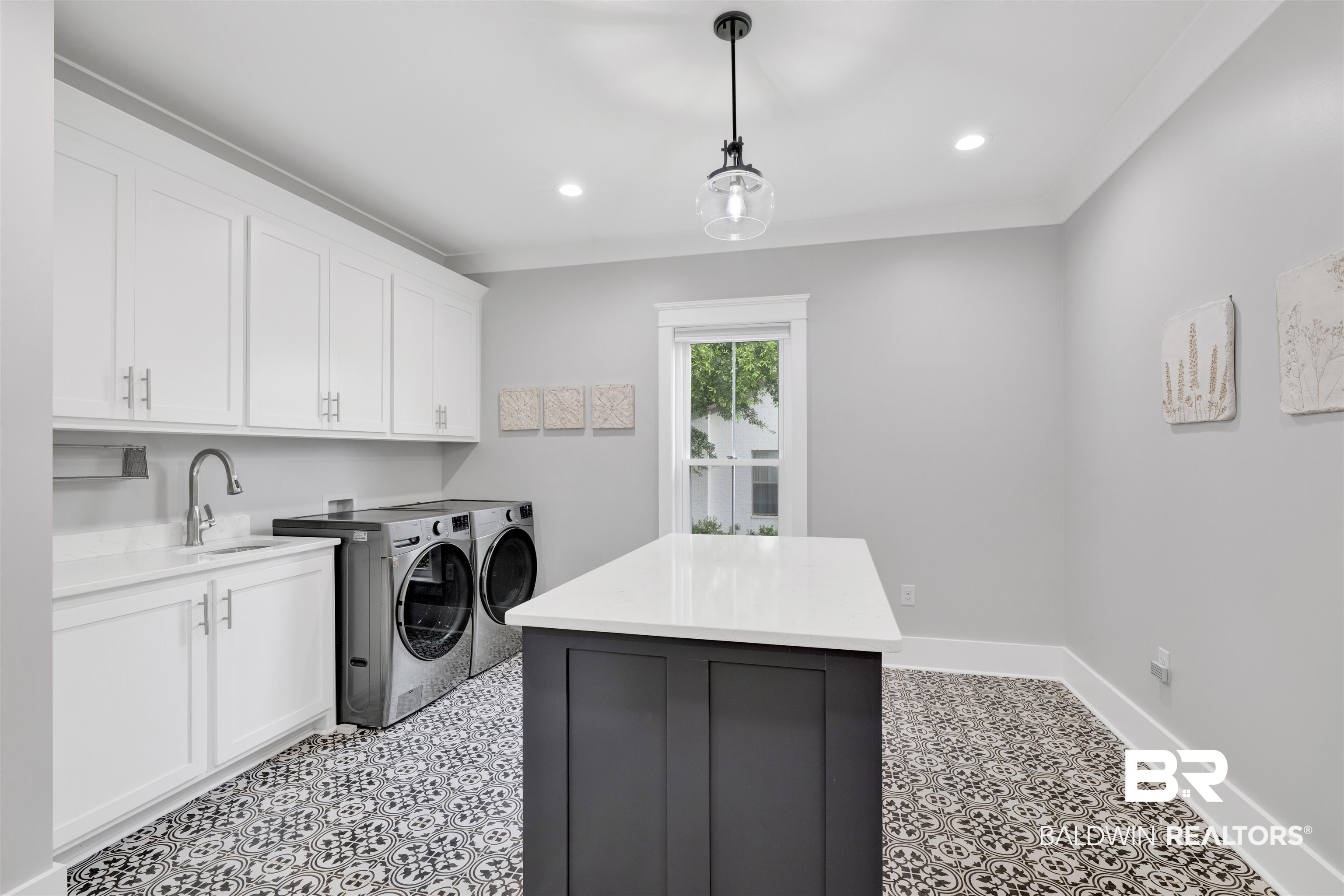 21702 Pillars Street Fairhope, AL 36532 - Photo 16 of 54 Laundry room featuring patterned floor tiles, white shaker cabinetry, a built-in sink with a gooseneck faucet, a light gray wall color, and a central island with a white countertop