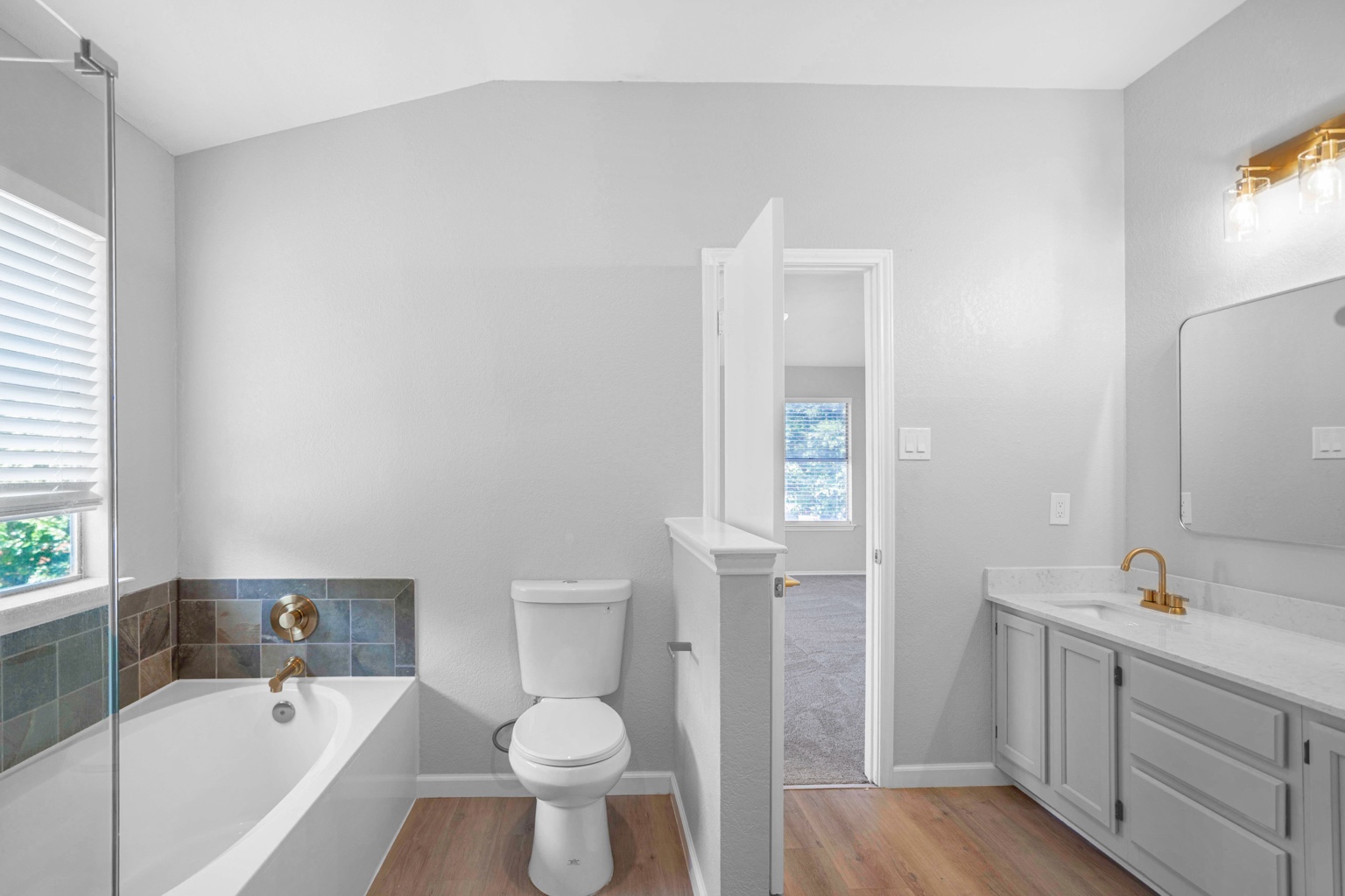 800 Smoke Signal Pass Pflugerville, TX 78660 - Photo 18 of 40 A pristine bathroom features a deep soaking tub with tile surround, a modern vanity, and light-toned wood-look flooring.