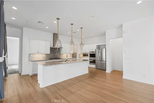 a kitchen with stainless steel appliances granite countertop a refrigerator a sink a stove and a wooden floors