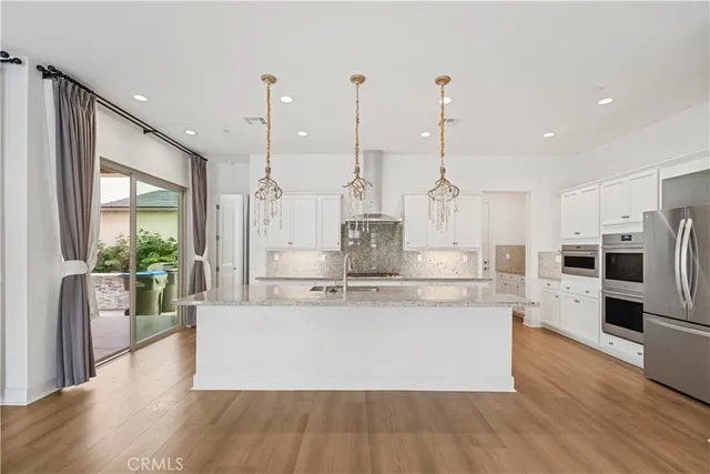 a view of kitchen with stainless steel appliances granite countertop a stove a refrigerator a oven and a wooden floor