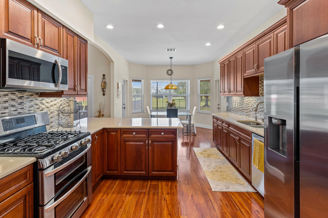 2774 Gentile Road Fort Pierce, FL 34945 - Photo 18 of 70 a kitchen with stainless steel appliances granite countertop a stove top oven a sink dishwasher and a refrigerator with wooden floor