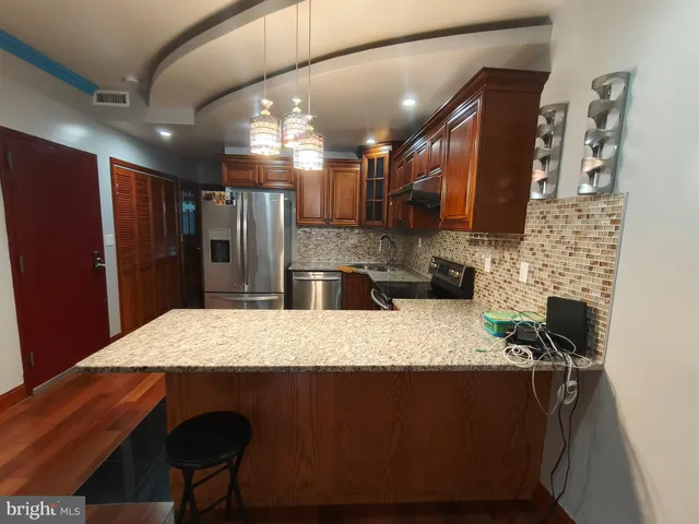 a kitchen with stainless steel appliances kitchen island granite countertop a refrigerator a stove and a sink with wooden floor