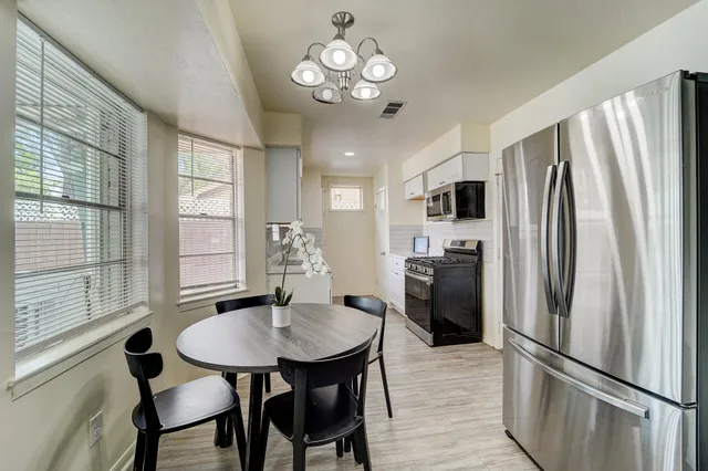 a kitchen with stainless steel appliances granite countertop a refrigerator a sink dishwasher a dining table and chairs with wooden floor