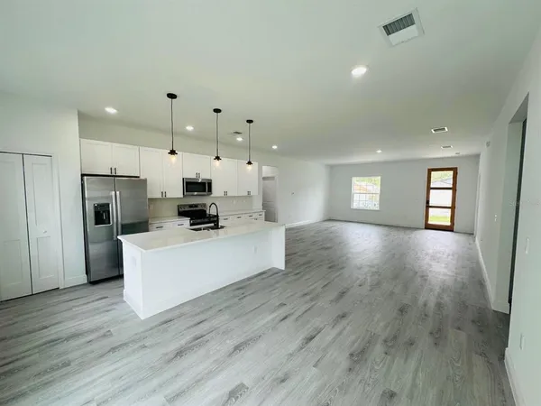 a living room with stainless steel appliances kitchen island wooden floors and white walls