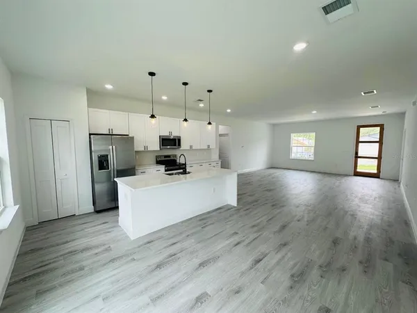 a large white kitchen with kitchen island a refrigerator a sink dishwasher and a stove with wooden floor