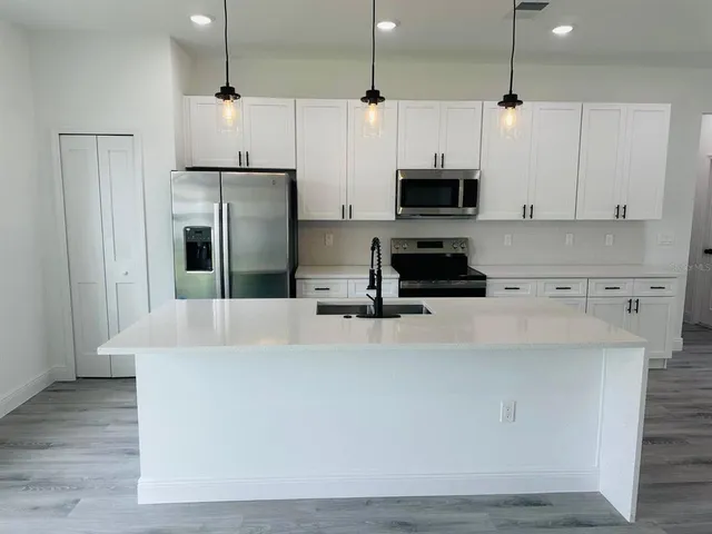 a kitchen with stainless steel appliances a stove a refrigerator a sink and white cabinets