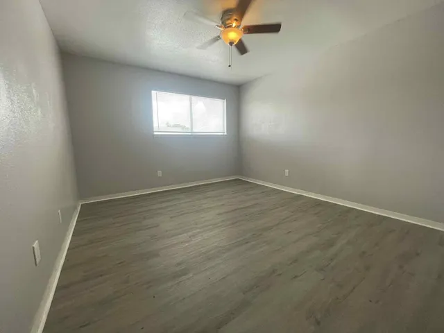 an empty room with wooden floor fan and windows