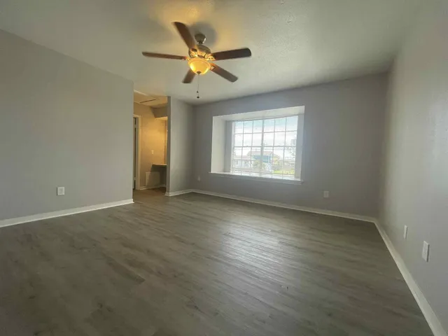 an empty room with wooden floor fan and windows
