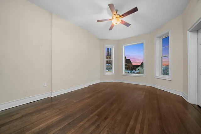 an empty room with wooden floor chandelier fan and windows
