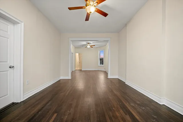an empty room with wooden floor chandelier fan and windows