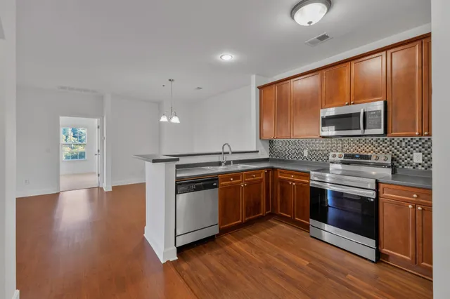 a kitchen with stainless steel appliances granite countertop a refrigerator a stove and a sink with wooden floors