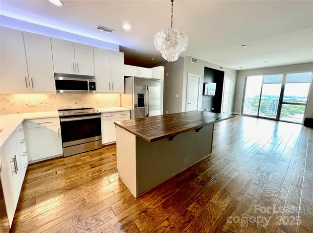 a kitchen with stainless steel appliances granite countertop a refrigerator a stove oven a sink dishwasher and white cabinets with wooden floor