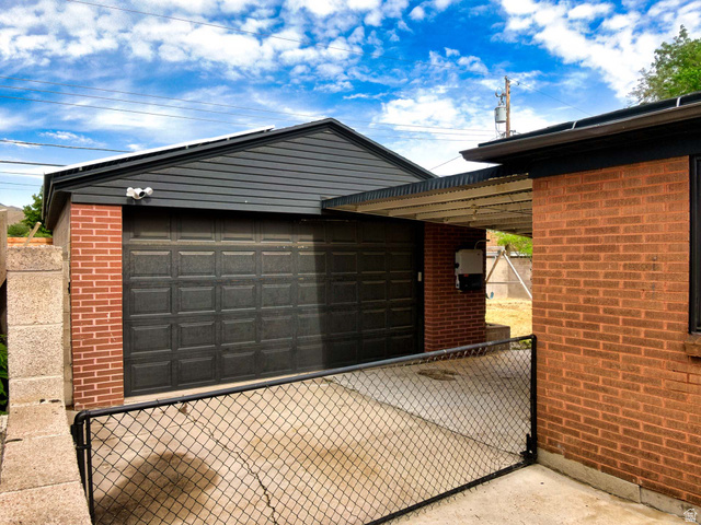 3138 Jean Street Magna, UT 84044 - Photo 26 of 26 Attached single-car garage featuring a dark panel door, brick facade, and an integrated carport structure