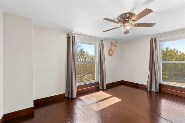 an empty room with wooden floor fan and windows