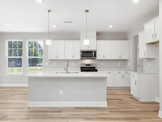 a large white kitchen with a large island oven a sink stainless steel appliances and cabinets
