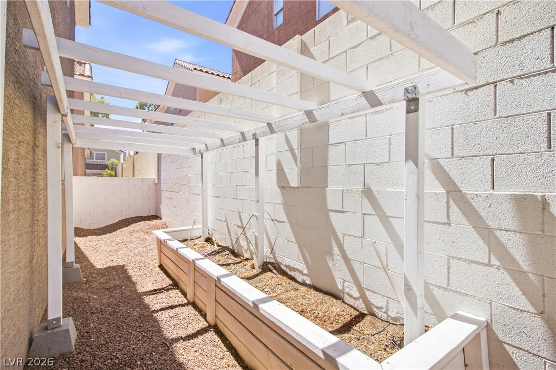1475 Reef Ridge Court Las Vegas, NV 89128 - Photo 19 of 24 Raised planter beds sit beneath a white wooden pergola in the side yard.