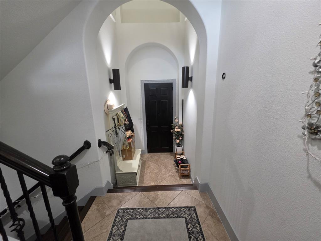 809 Rockingham Drive Irving, TX 75063 - Photo 8 of 30 Arched entryway with a dark wood-finish door, tile flooring with decorative inlay, and a dark wood-finish handrail with metal balusters