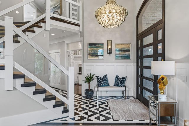 12308 Mariah Circle Draper, UT 84020 - Photo 22 of 293 Grand foyer featuring a custom glass and wood staircase, a modern statement chandelier, bold geometric flooring, wainscoting, and a multi-paneled entry door with an arched transom