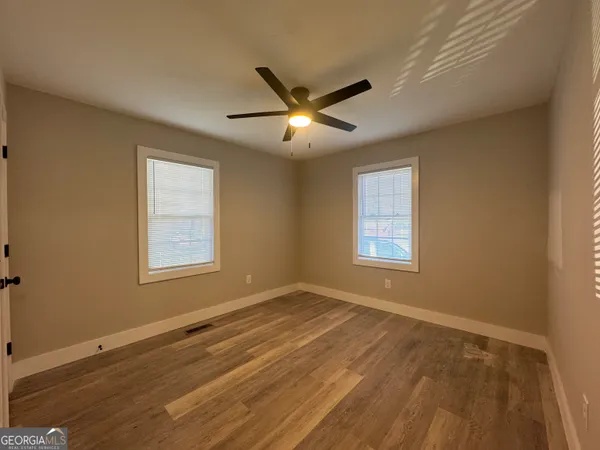an empty room with wooden floor ceiling fan and windows