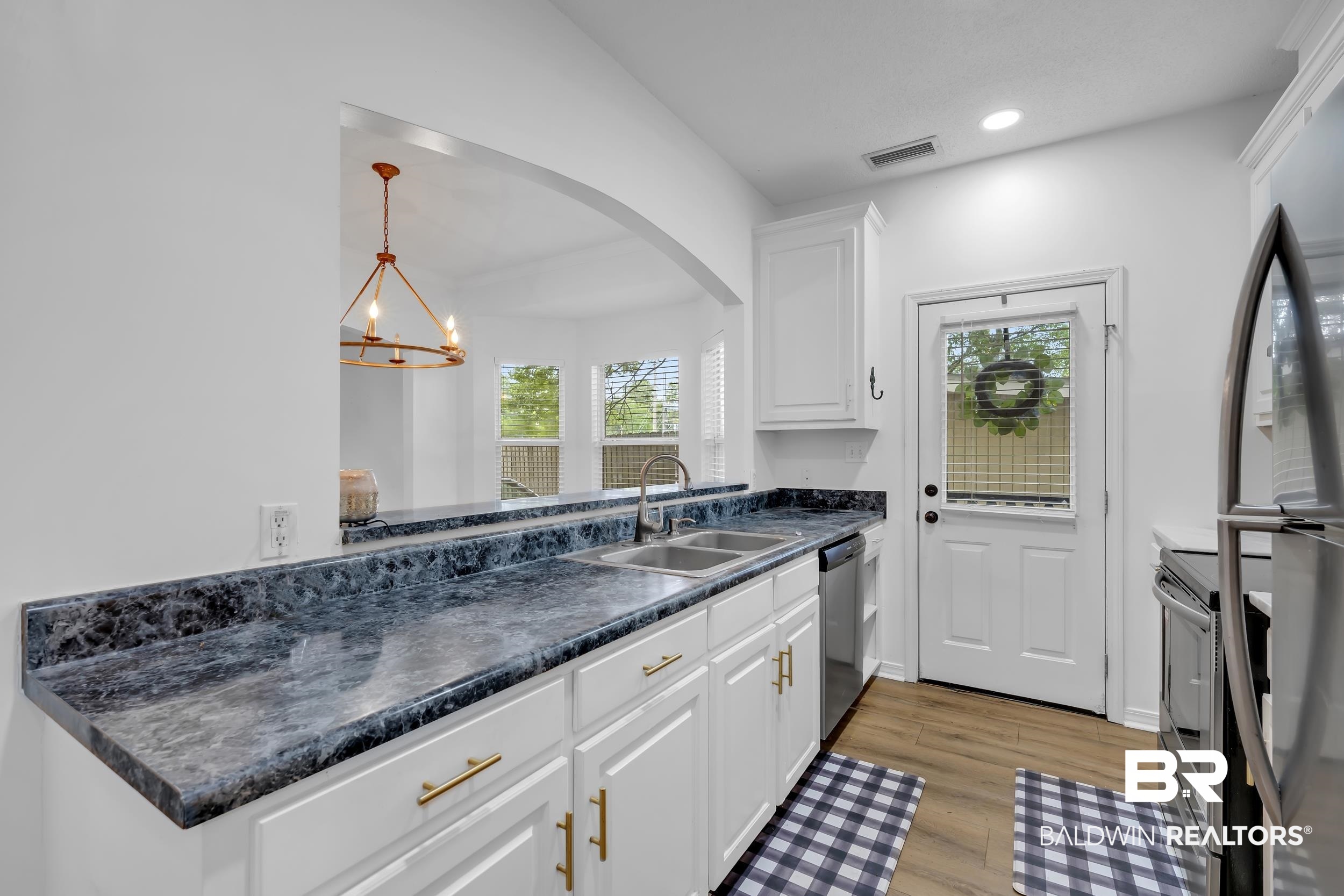 17488 Pandion Ridge, Unit A1 Fairhope, AL 36532 - Photo 10 of 18 Kitchen featuring white cabinetry with gold-toned hardware, dark patterned countertops, a double-basin sink, and integrated stainless steel appliances