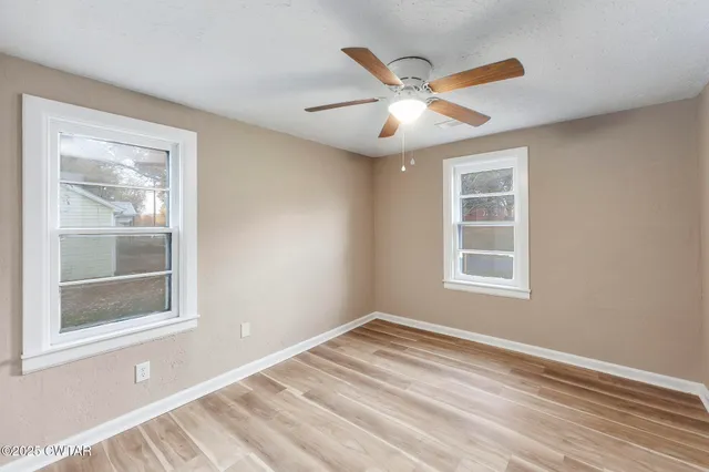 a view of an empty room with a window and wooden floor