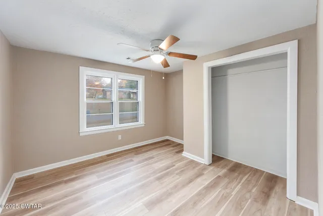 a view of empty room with wooden floor and fan