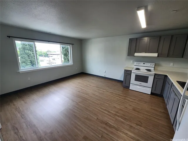 an empty room with wooden floor kitchen view and a window