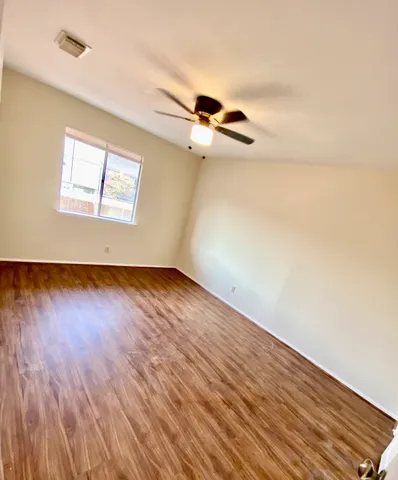 an empty room with wooden floor ceiling fan and windows
