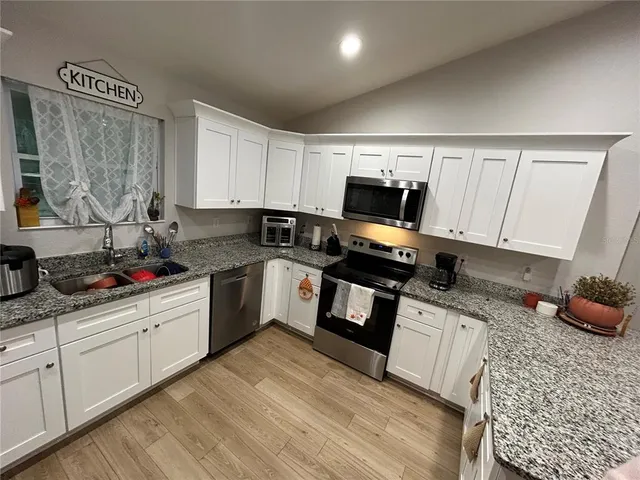 a kitchen with granite countertop a stove a sink dishwasher and a microwave oven with white cabinets