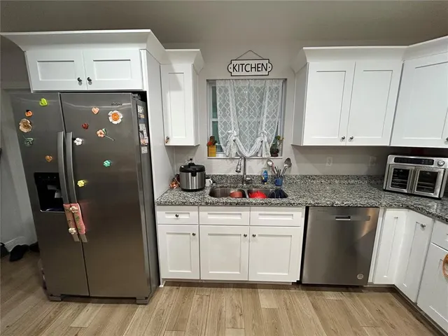 a kitchen with stainless steel appliances granite countertop a refrigerator a sink dishwasher and white cabinets with wooden floor