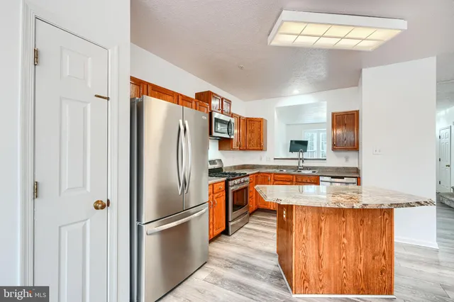 a kitchen with stainless steel appliances granite countertop a refrigerator a sink dishwasher a stove and a dining table with wooden floor